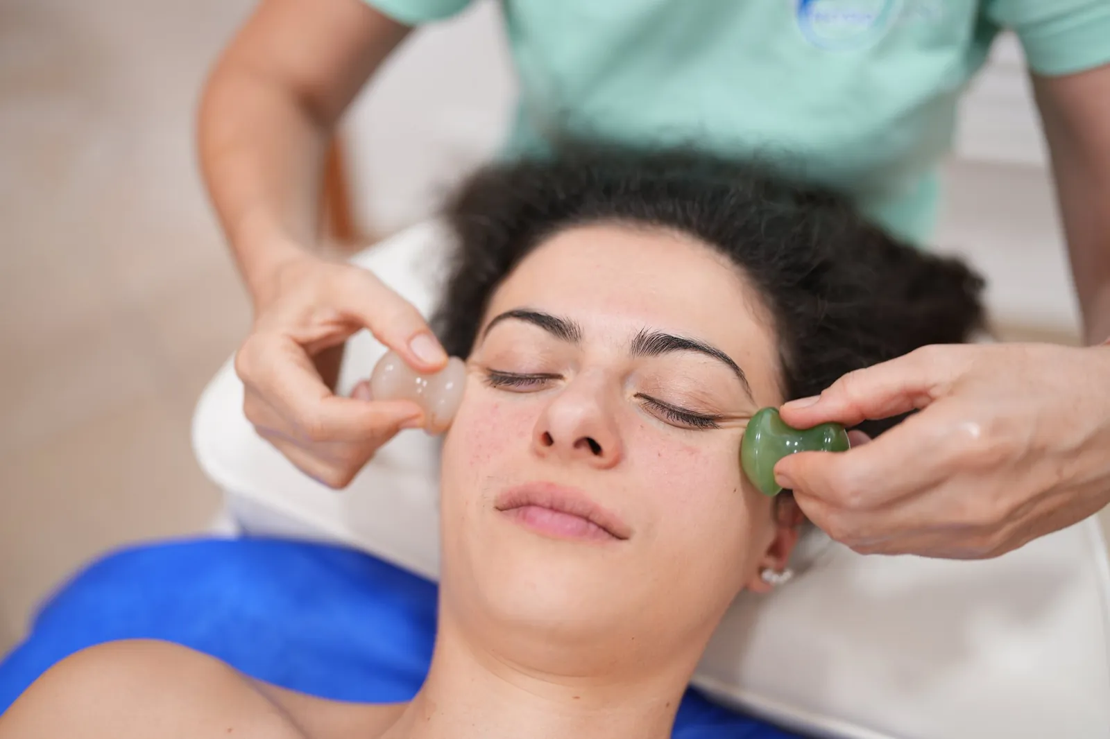 Fasciális arckezelés: a terapeuta két masszázskővel kezeli a kliens arcát