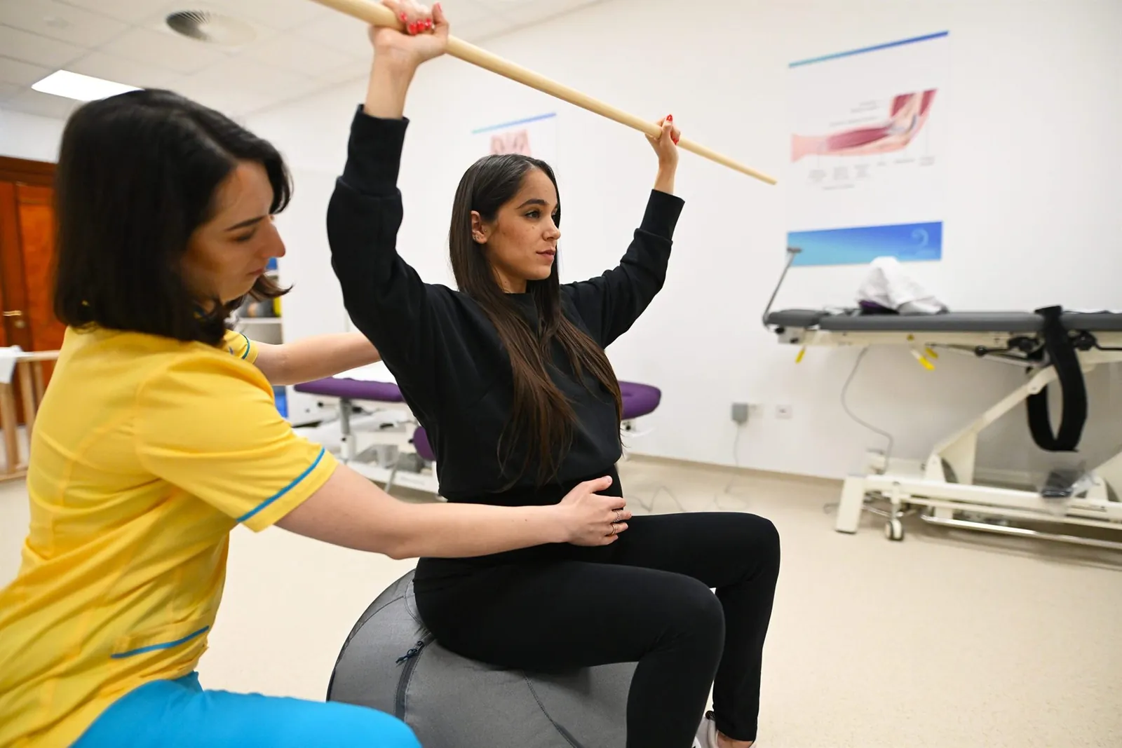 Kismama gyógytornász irányításával végez gyakorlatot fitneszlabdán